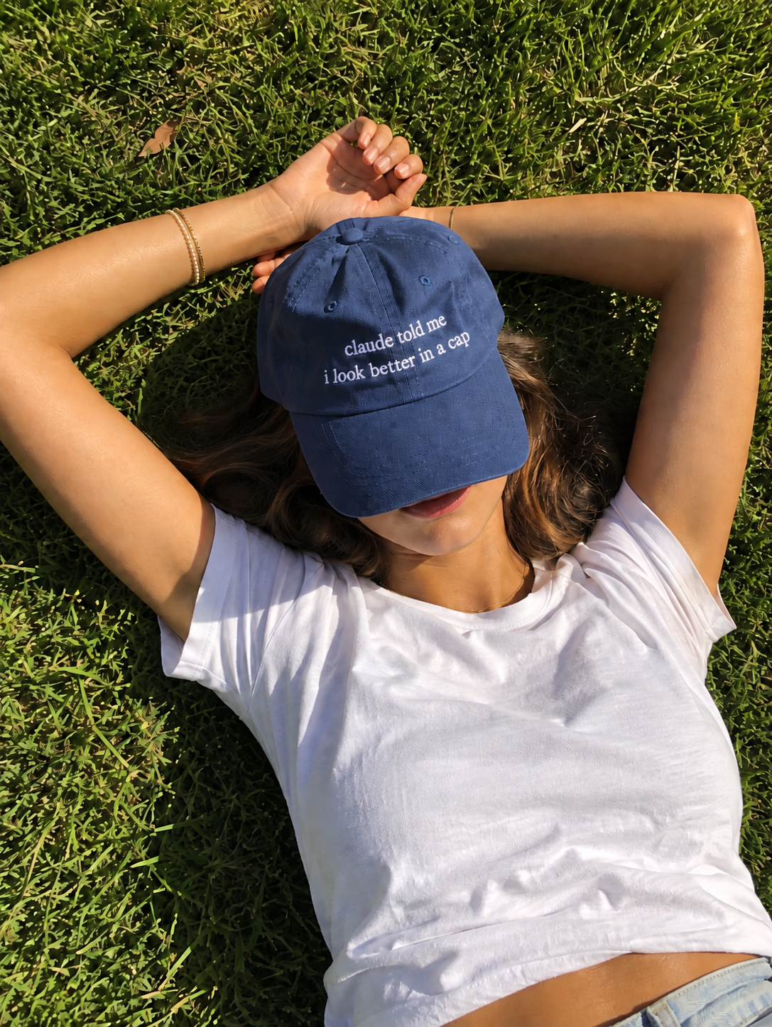 ChatGPT result: person lying in grass with arms above their head wearing a navy cap that reads claude told me i look better in a cap
